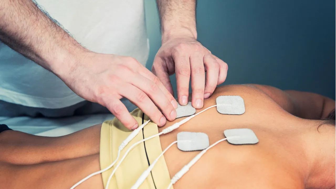 Kéz TENS-elektródákat helyez egy páciens derekára