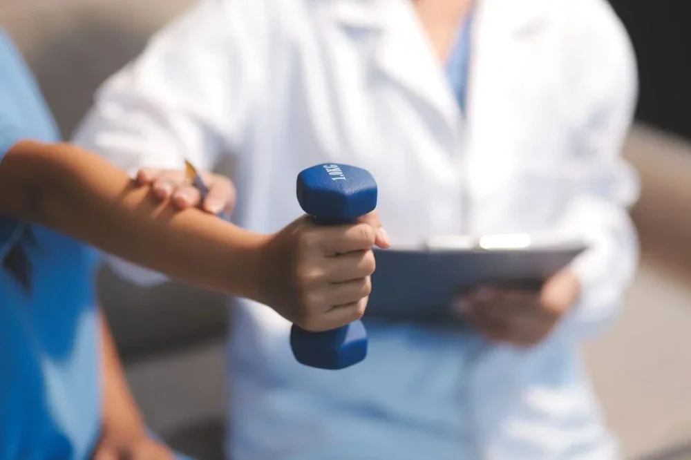 Jegyzetelő terapeuta, előtte kézi súlyzót tartó páciens keze (illusztráció)