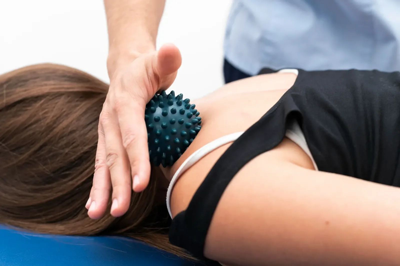 Tüskés masszázslabda egy fekvő nő lapockáján, fölötte a terapeuta keze (illusztráció)